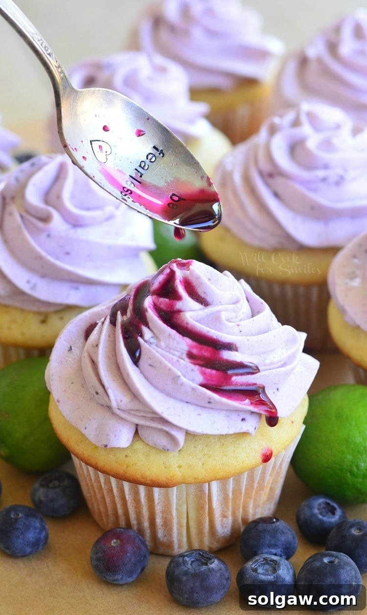 Tangy Blueberry Key Lime Delights 3 spooning sauce over cupcakes with Fresh Blueberry Cream Cheese Frosting on a cutting board with blueberries and limes
