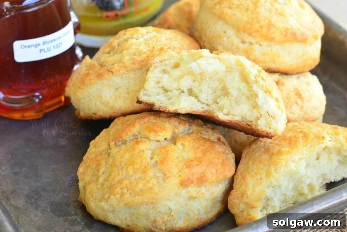 honey butter biscuits with on a baling sheet with one cut in half and honey also on the baking sheet.