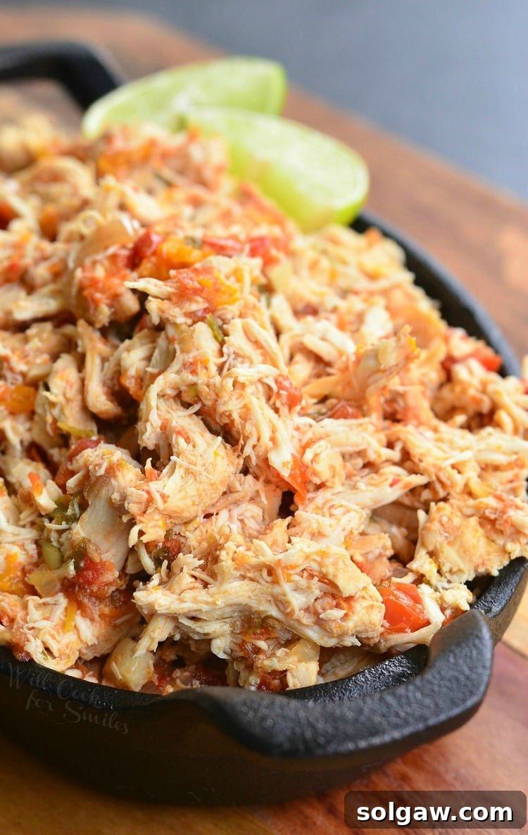 Fiesta Slow Cooker Salsa Chicken 2 Black skillet filled with crock pot shredded salsa chicken on a wooden cutting board with a lime garnish along the side of the skillet