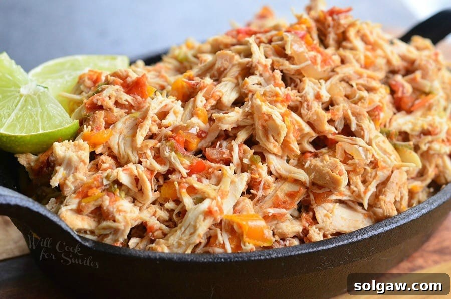 Fiesta Slow Cooker Salsa Chicken 7 Close up view of crock pot shredded salsa chicken on a black skillet with a lime garnish on a wooden cutting board