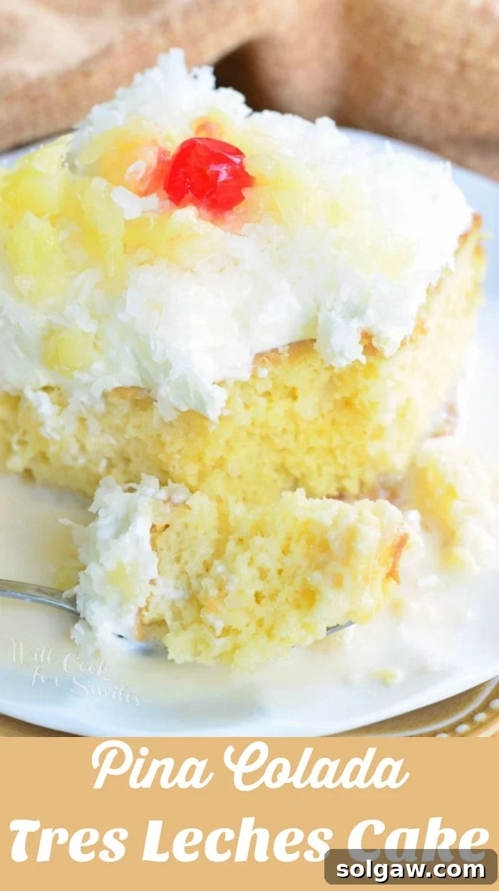 A close-up of a slice of Pina Colada Tres Leches Cake, featuring its moist, milky layers, fluffy coconut frosting, and generous pineapple and cherry garnishes.