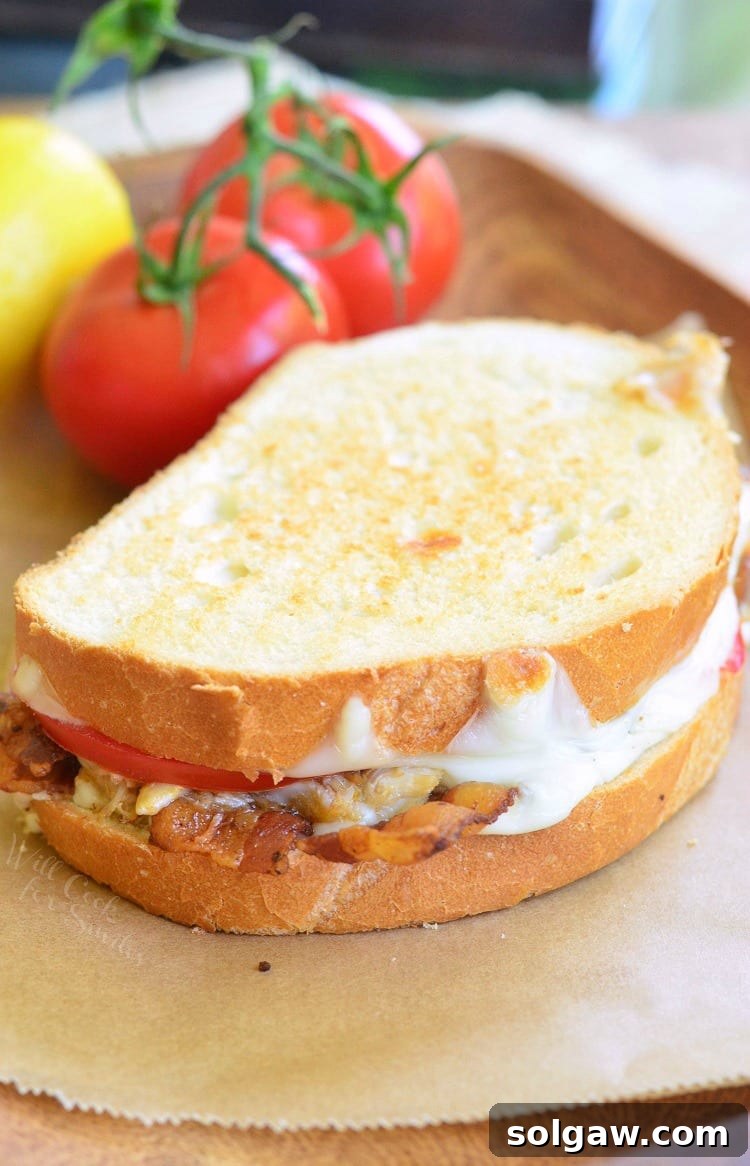 Delicious Crab Grilled Cheese sandwich with tomatoes and bacon, served on parchment paper with fresh vine tomatoes in the background
