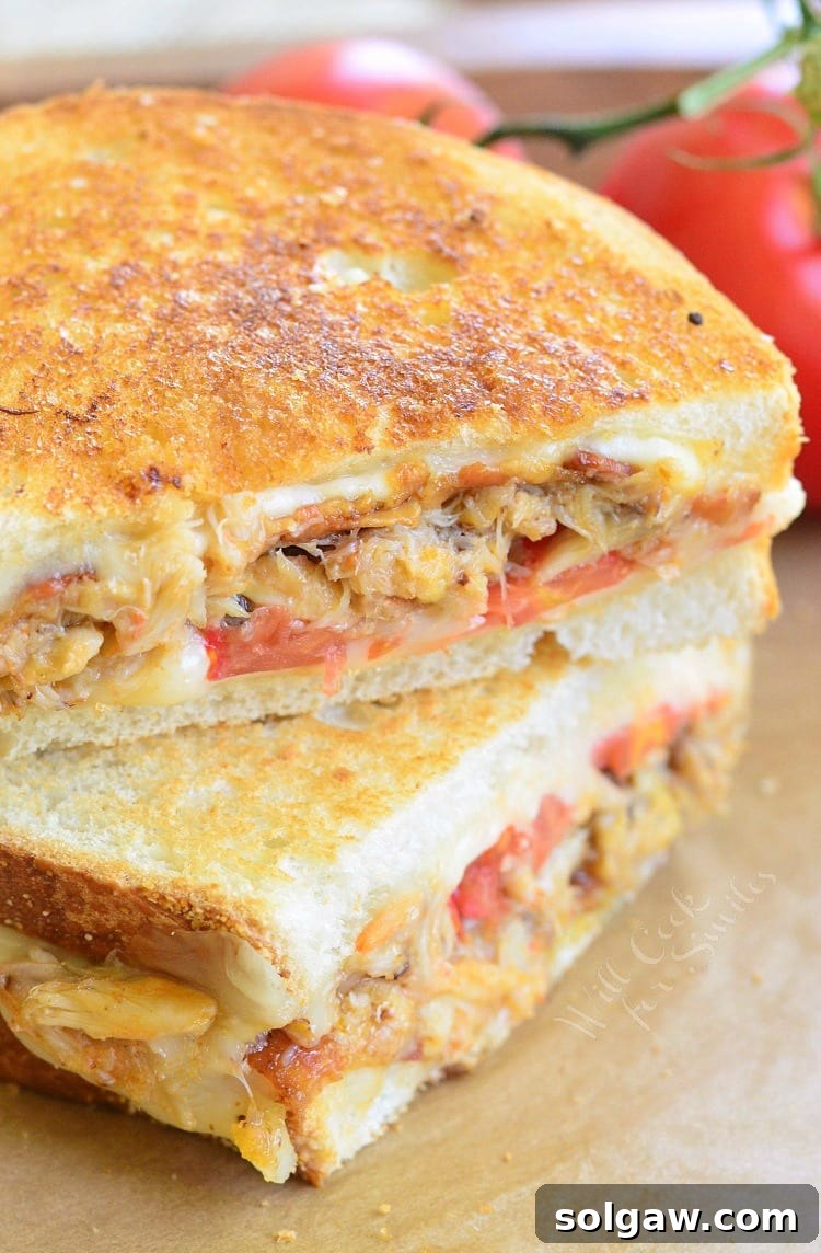 Crab Grilled Cheese sandwich, cut in half to reveal layers of crab, cheese, bacon, and tomato, on parchment paper