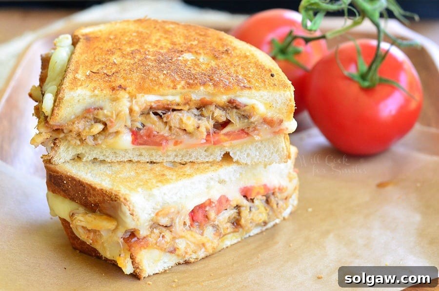 Close-up of Crab Grilled Cheese showing melted cheese, crab, bacon, and tomato layers