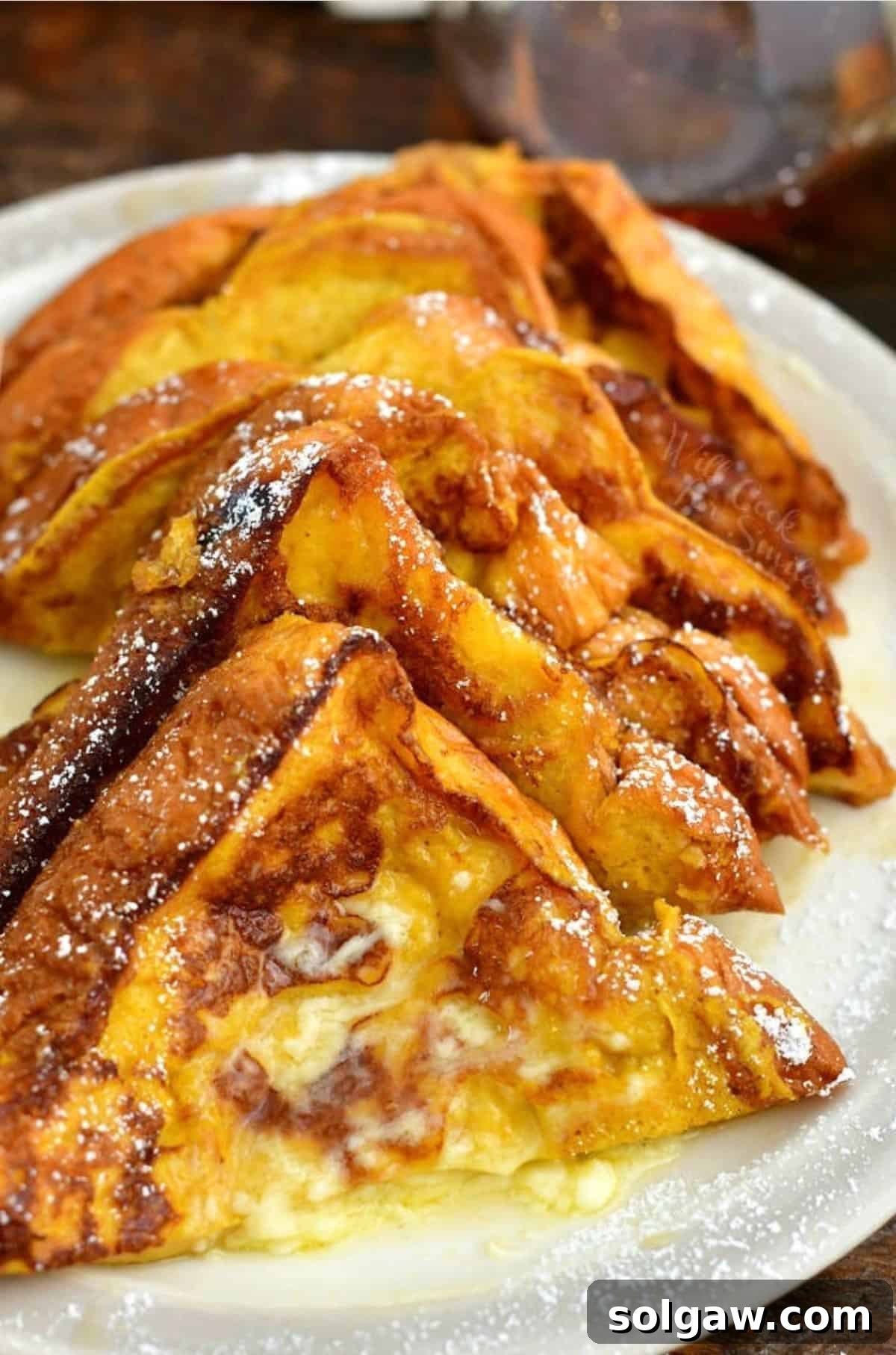 Spiced Pumpkin French Toast 8 Pumpkin French toast slices cut in half and stacked on the plate with butter and powdered sugar.
