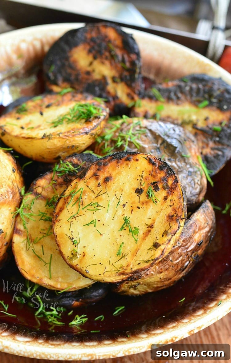 Herbed grilled potatoes on a brown and white platter on a wooden table topped with dill