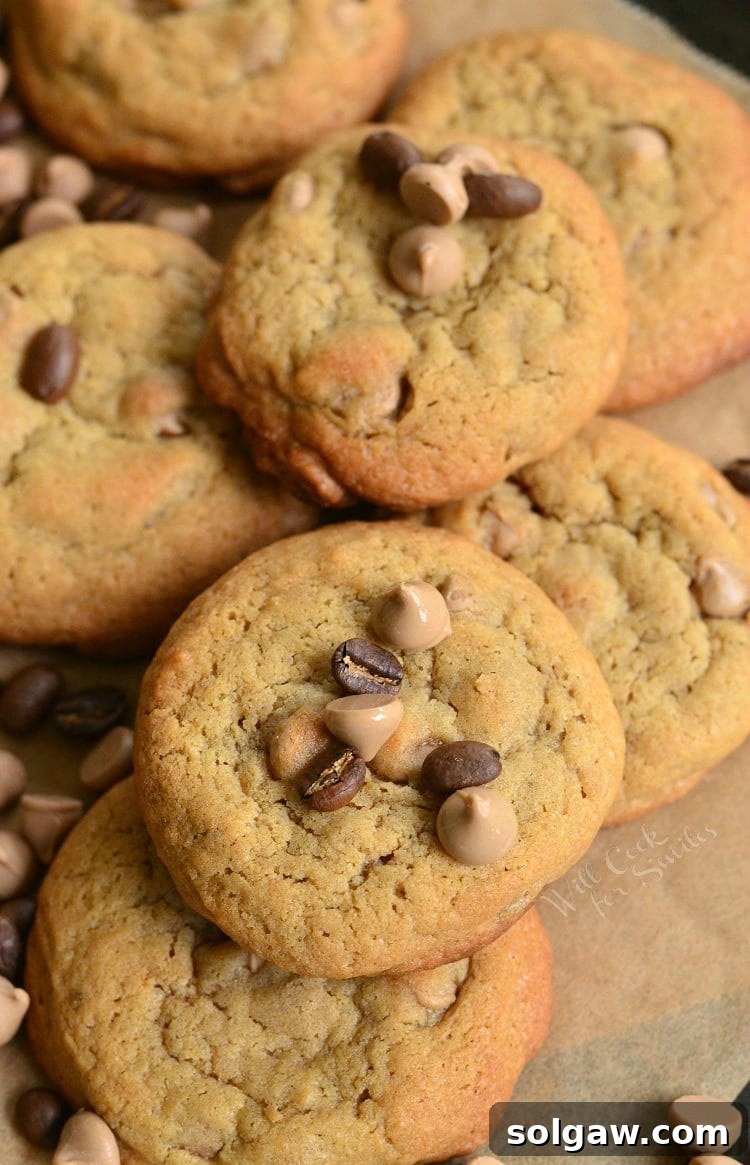 Cappuccino Cookies stacked up on parchment paper with chocolate chips and cappuccino chips around it and ontop