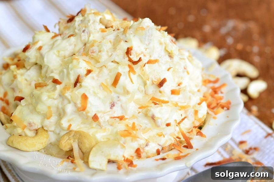 Close-up shot of Toasted Coconut Cashew Fluff Salad in a white bowl, showcasing the generous topping of golden toasted coconut and chopped cashews, highlighting its inviting texture.