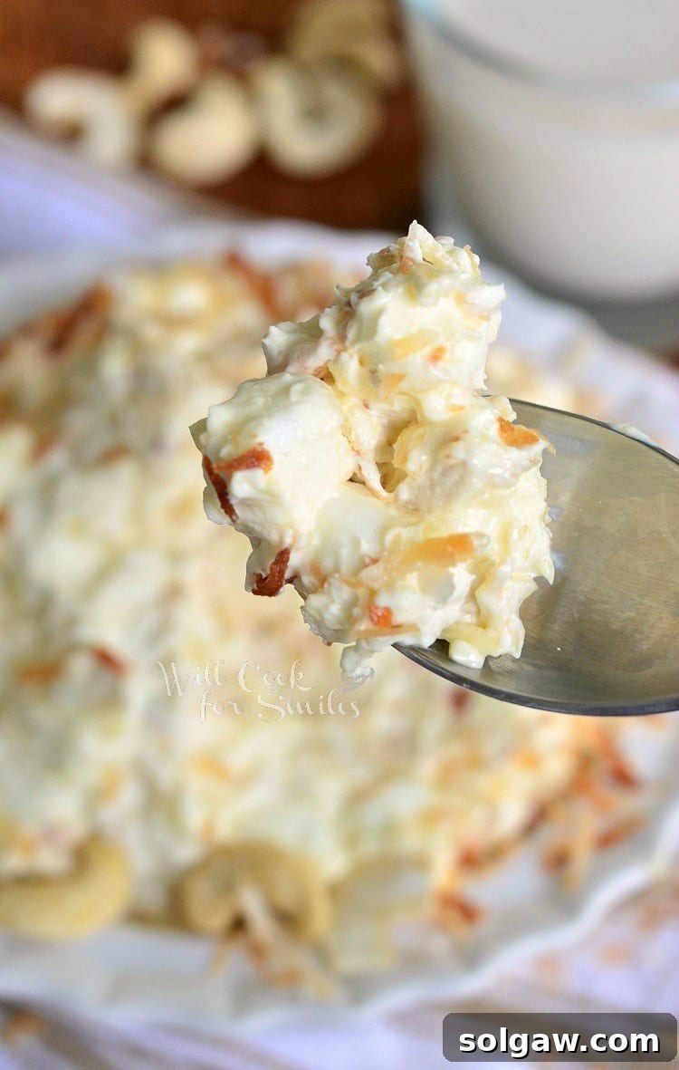 A spoon full of the creamy Toasted Coconut Cashew Fluff Salad, freshly scooped from a white bowl, ready to be enjoyed.