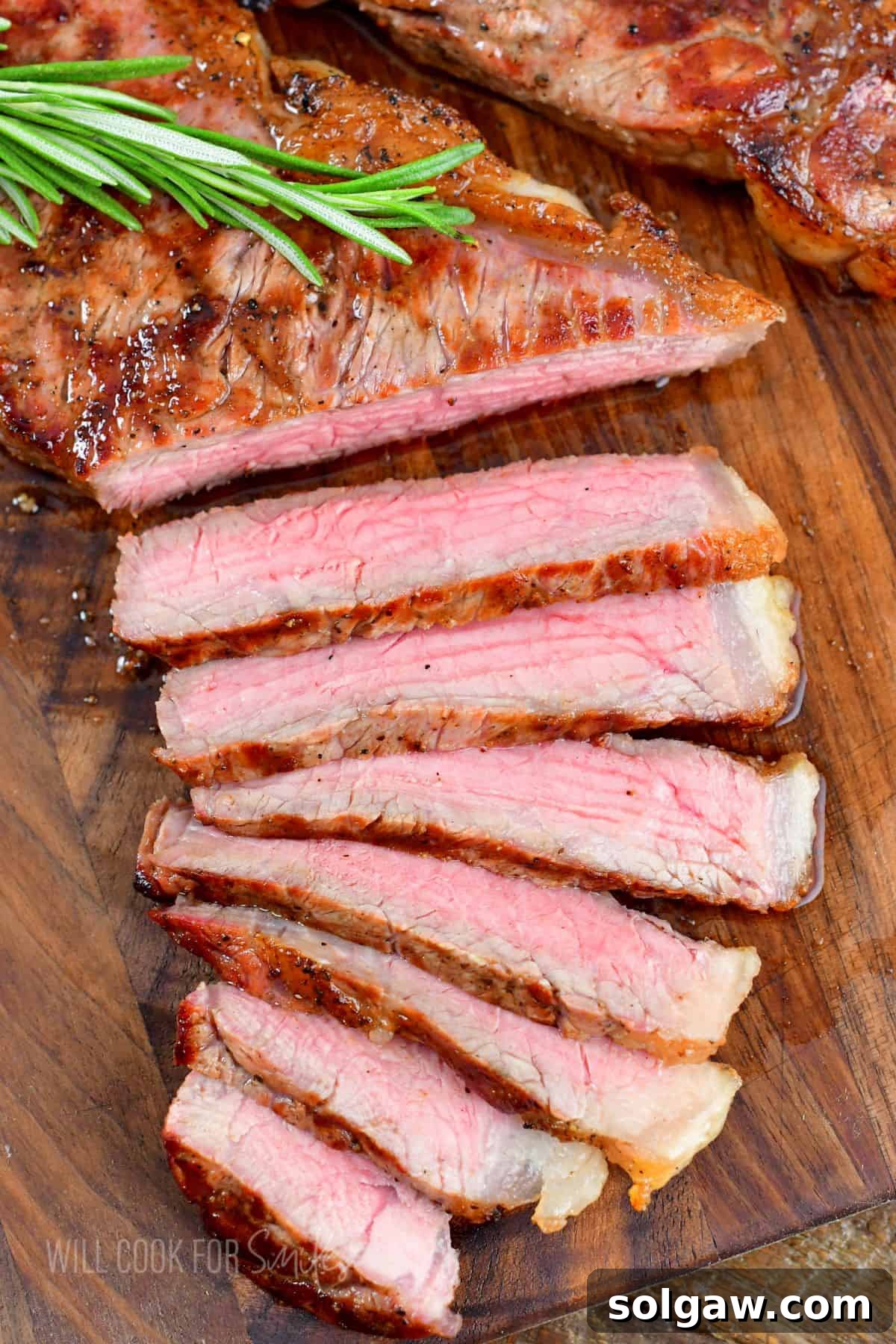 The Art of Grilling Perfect Steaks 2 Perfectly grilled steak slices on a wooden cutting board next to a larger piece of steak, garnished with fresh rosemary.