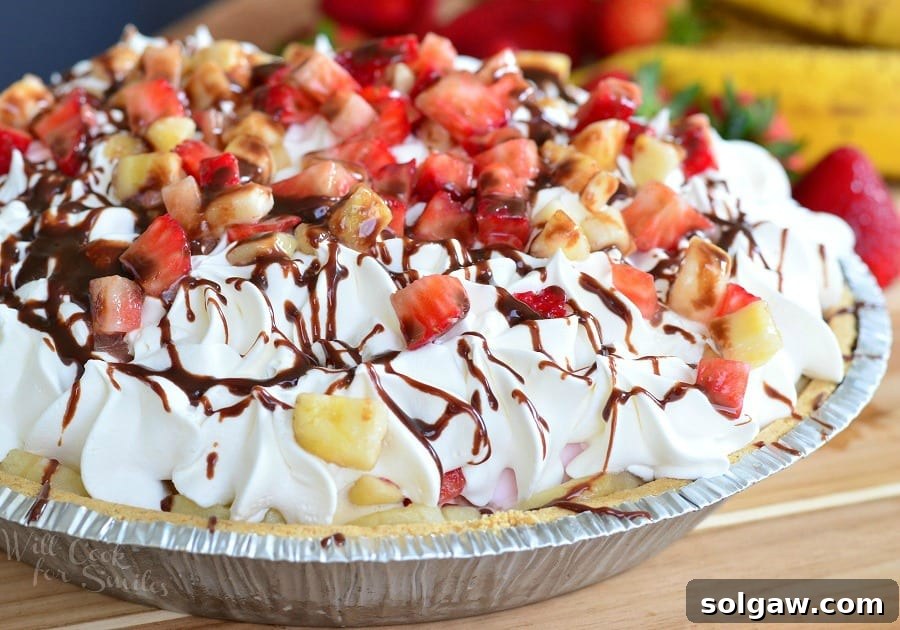 Banana Split Ice Cream Pie on a wooden table with bananas and strawberries in the background as viewed close up