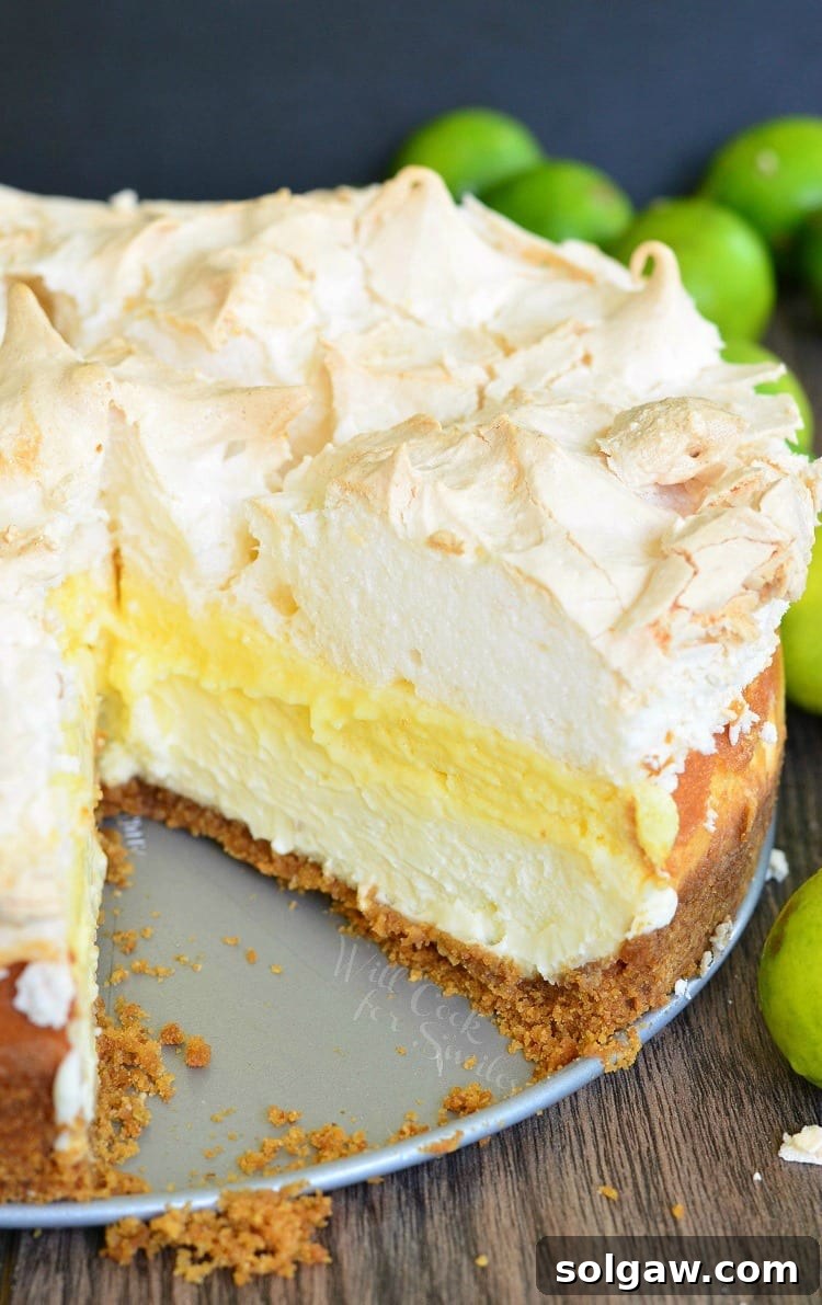 A slice missing from a whole Key Lime Pie Cheesecake with fresh limes in the background, showing the rich layers and meringue.