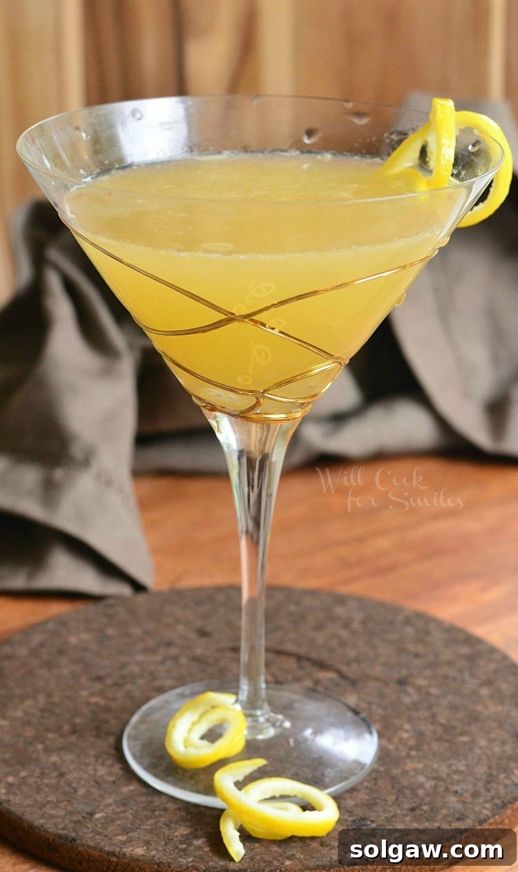 A vibrant Pineapple Lemon Martini, elegantly served in a martini glass with decorative gold swirls and garnished with a delicate lemon peel, radiating freshness.