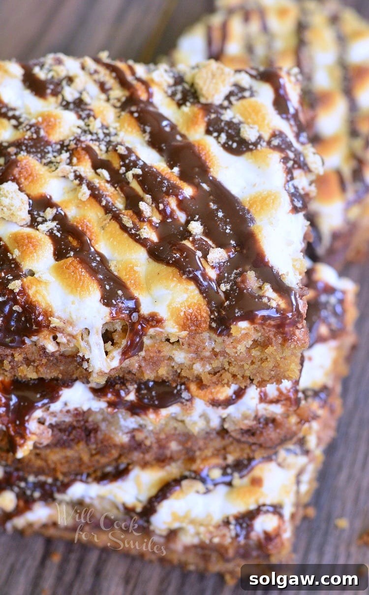 3 layered double chocolate S'Mores crumble cookie bars stacked on top of each other on a dark wooden table as viewed from above