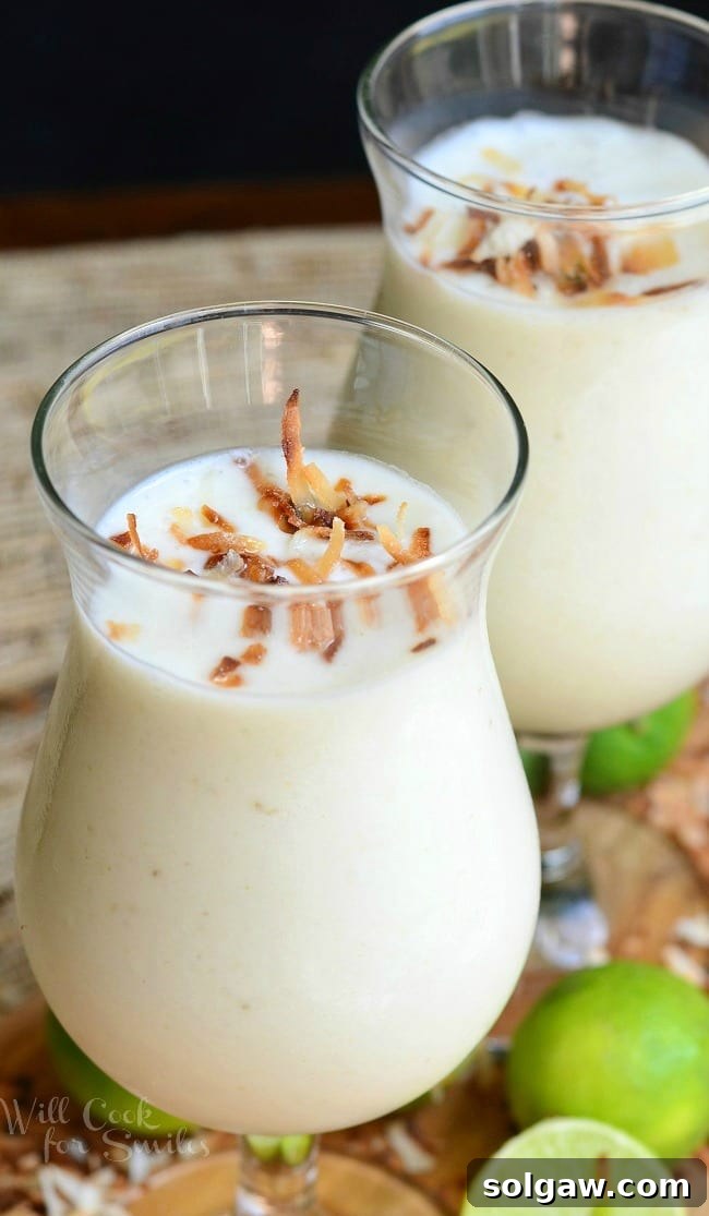 A tall, clear glass filled with a creamy tropical smoothie, garnished with toasted coconut flakes, ready to be enjoyed.