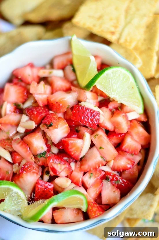 A bowl of fresh strawberry salsa, garnished with lemon and lime wedges, served alongside crispy cinnamon sugar chips, perfect for a sweet dessert.