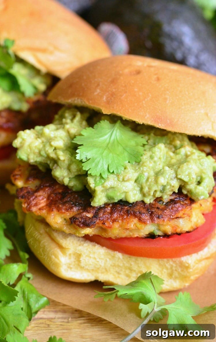 Shrimp Burgers on a bun with mashed avocado and cilantro on top, served with a side
