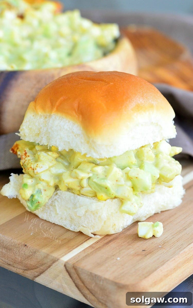 Avocado Cucumber Egg Salad served on a small dinner roll as a sandwich on a cutting board, garnished with herbs