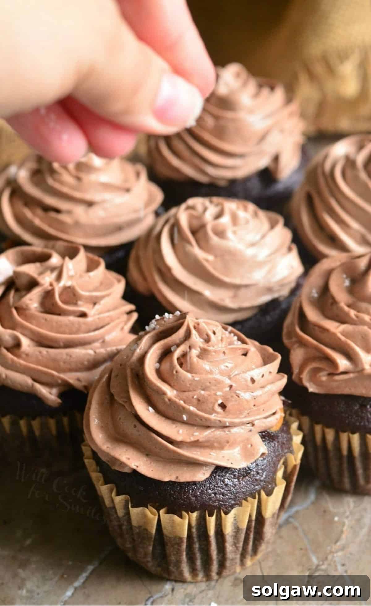 adding sprinkle of coarse salt on top of chocolate frosting on the cupcakes.