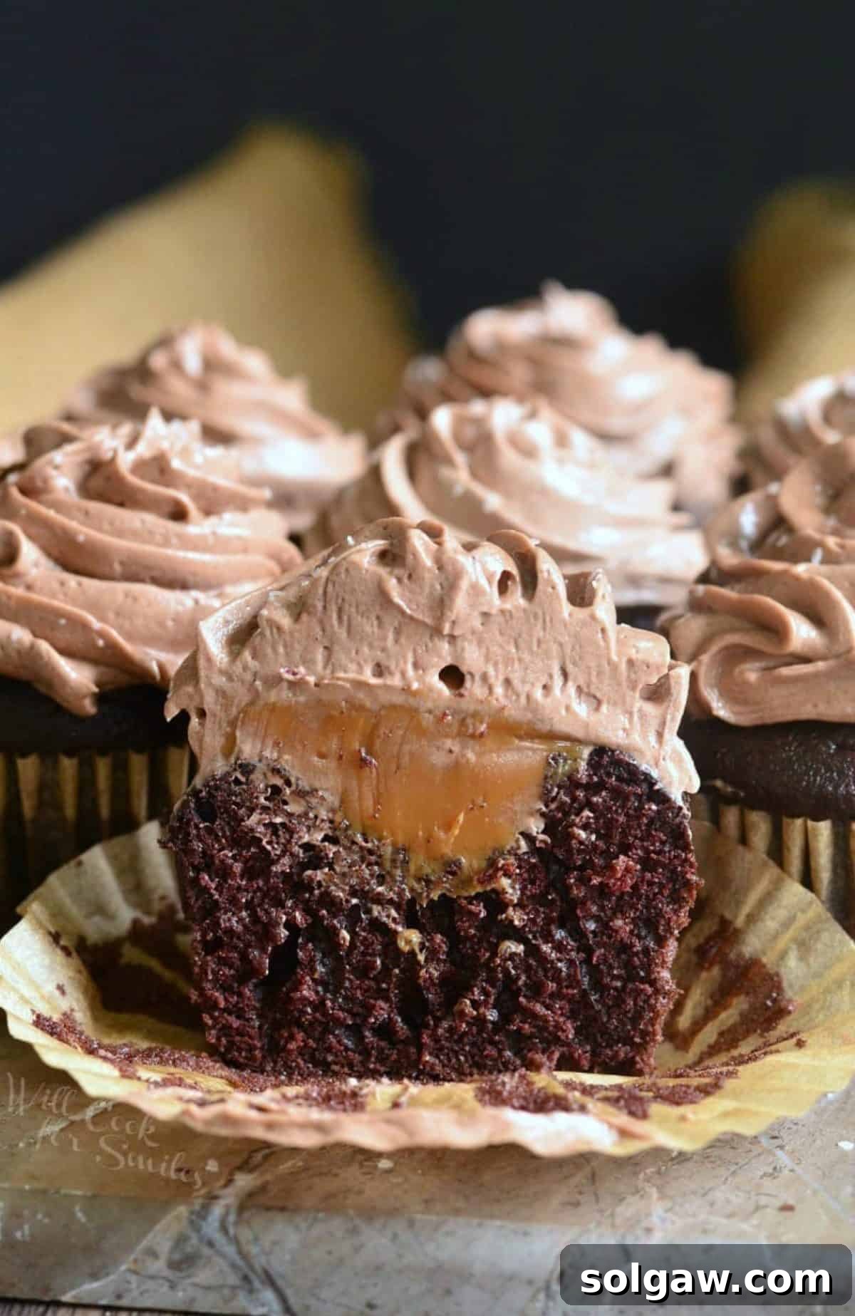 Chocolate cupcake with salted dulce de leche filling sitting on a stone counter with one cut in half.