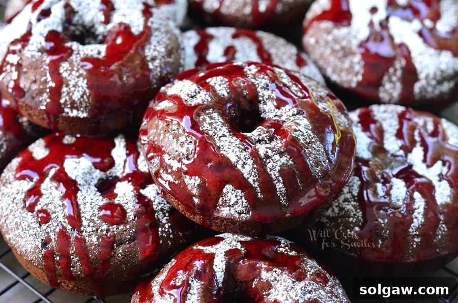 An array of Raspberry Chocolate Doughnuts, beautifully presented on a cooling rack, adorned with powdered sugar and a generous drizzle of raspberry sauce, ready to be enjoyed.