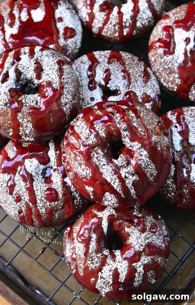 Raspberry chocolate doughnuts on a wire cooling rack topped with powdered sugar and raspberry glaze as viewed from above