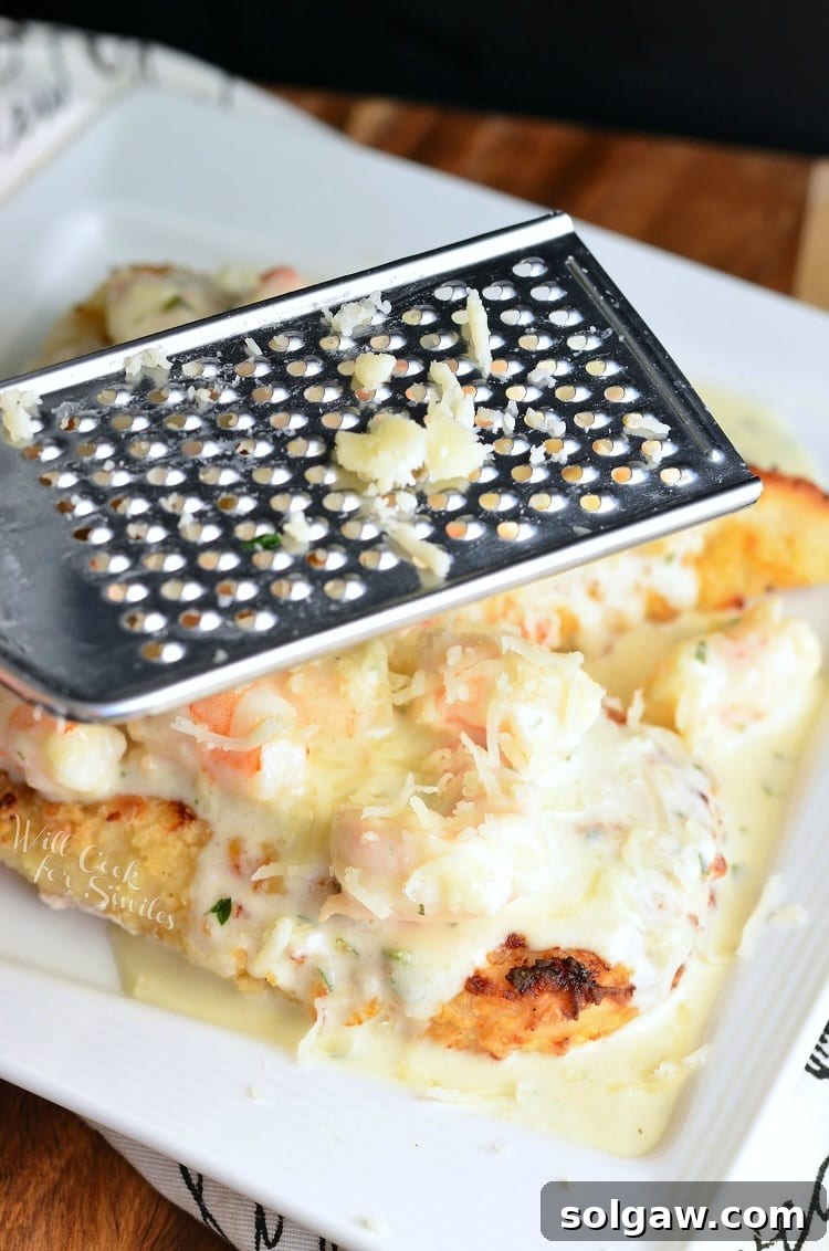 grating cheese with a cheese grater over Oven Fried Chicken topped with shrimp and a Creamy Fontina cheese Shrimp Sauce on a white plate