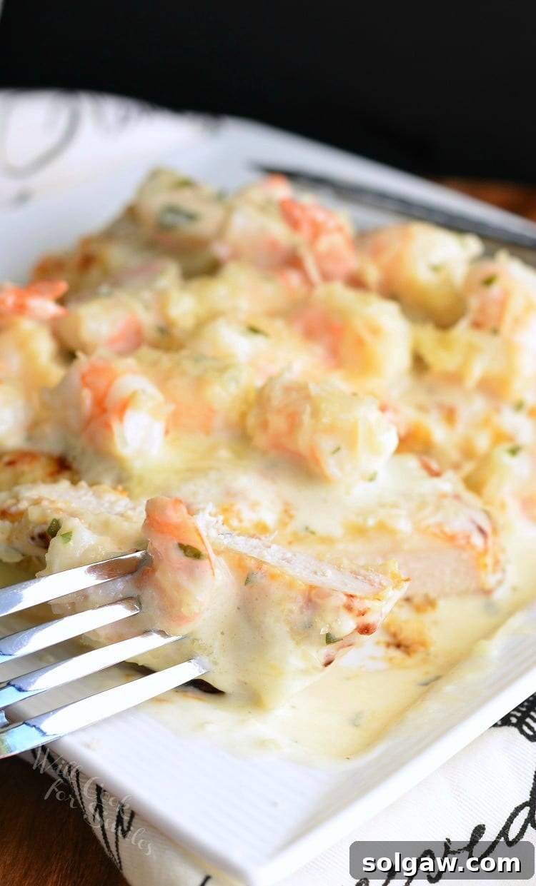Oven Fried Chicken topped with shrimp and a Creamy Fontina cheese Shrimp Sauce on a white plate with a fork in a piece to the left 