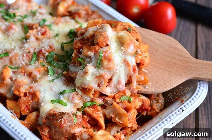 Hearty Chicken and Sausage Tortellini Bake 4 Chicken, Sausage, and pasta with cheese on top in a casserole dish with a wooden spoon lifting some out