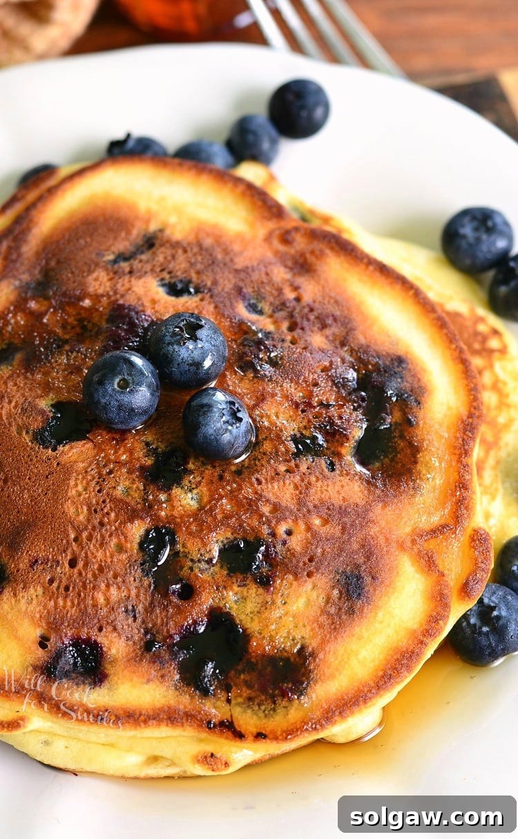 Single serving buttermilk pancakes topped with syrup and blueberries on a white plate with a fork in the background to the right.