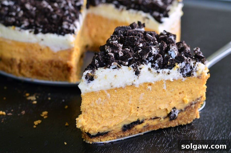 Decadent Layered Oreo Pumpkin Cheesecake 4 Layered Oreo Pumpkin Cheesecake slice on a pie cutter with the rest of the pie in the background