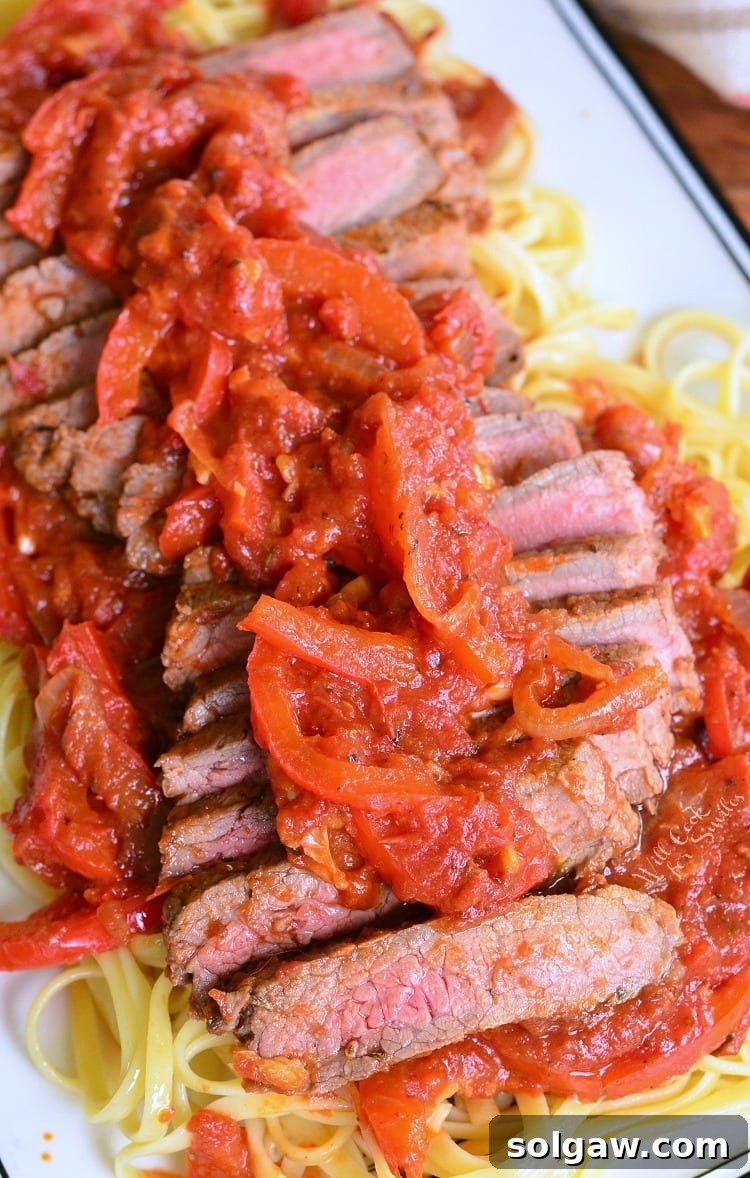 Rustic Steak Pizzaiola Linguine 9 Steak Pizzaiola Linguine artfully arranged on a plate with vibrant onion and tomato sauce visible, garnished with fresh herbs.