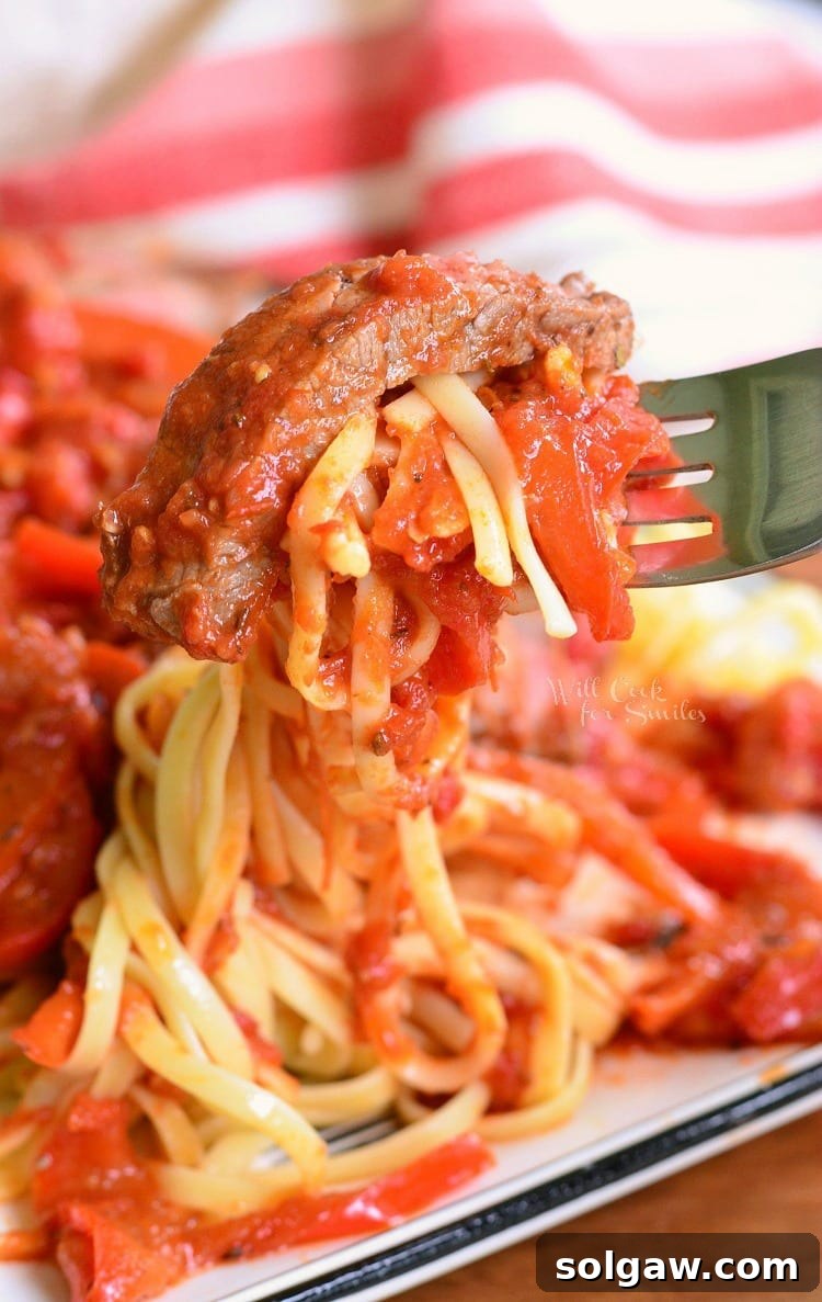 Rustic Steak Pizzaiola Linguine 3 A fork lifting a piece of Steak Pizzaiola from a white plate, showcasing the rich sauce and linguine underneath.