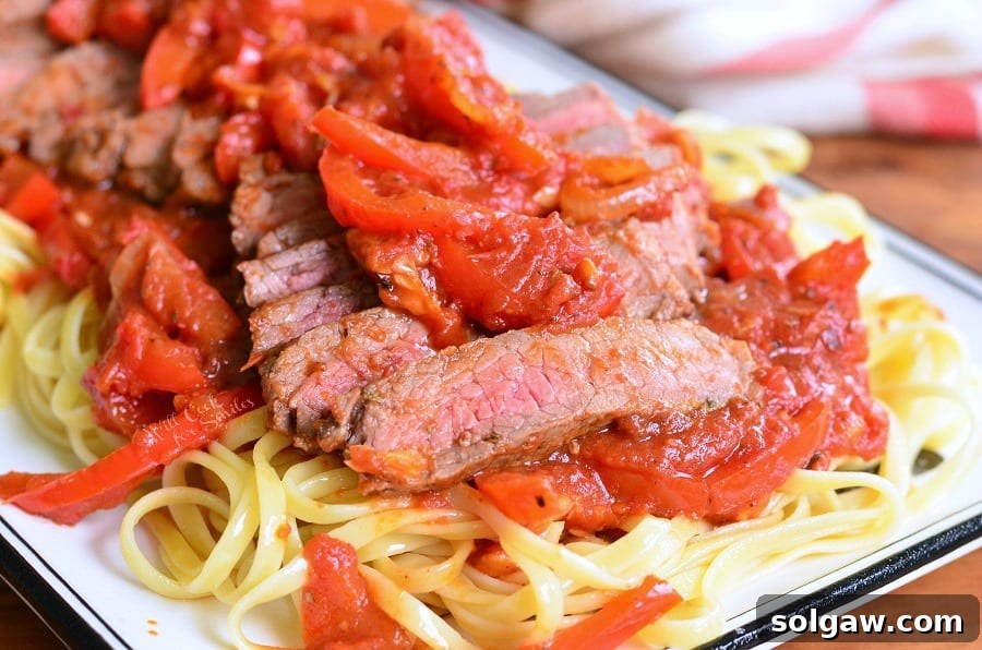 Decorative white rectangular plate with Steak Pizzaiola Linguine on a wooden table, viewed close-up.