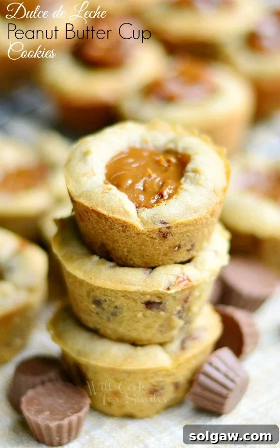 Stack of rich Dulce De Leche Peanut Butter Cup Cookies with mini Reese's cups scattered around, tempting any sweet tooth.