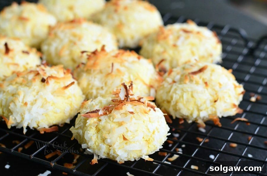 Three golden Coconut Pudding Cookies, one bitten to reveal its soft interior, garnished with toasted coconut flakes, resting on a cooling rack.