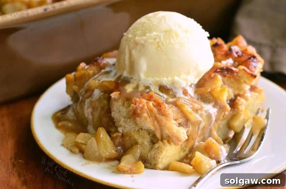 A tempting slice of apple pie bread pudding on a plate, adorned with a scoop of vanilla ice cream and a fork ready to dig in.