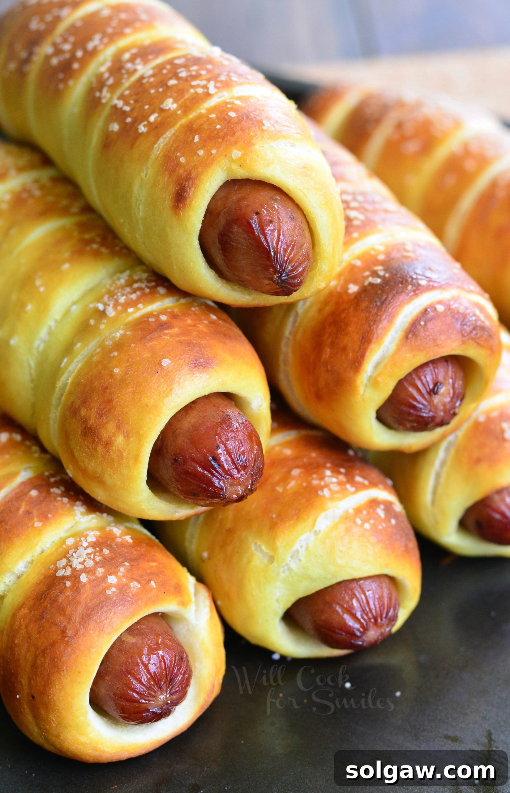 Close up of perfectly golden brown Pretzel Wrapped Hot Dogs stacked on a baking sheet