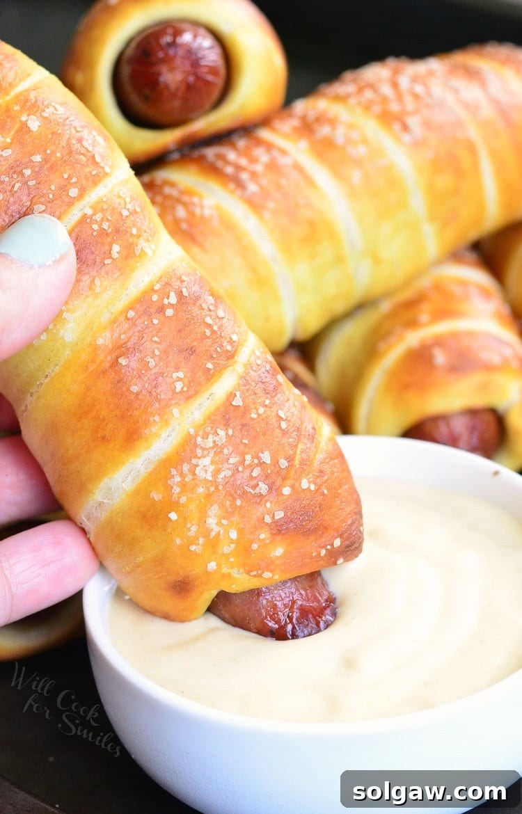 Dipping a Pretzel Wrapped Hot Dog into creamy Maple Dijon Dipping Sauce in a white bowl