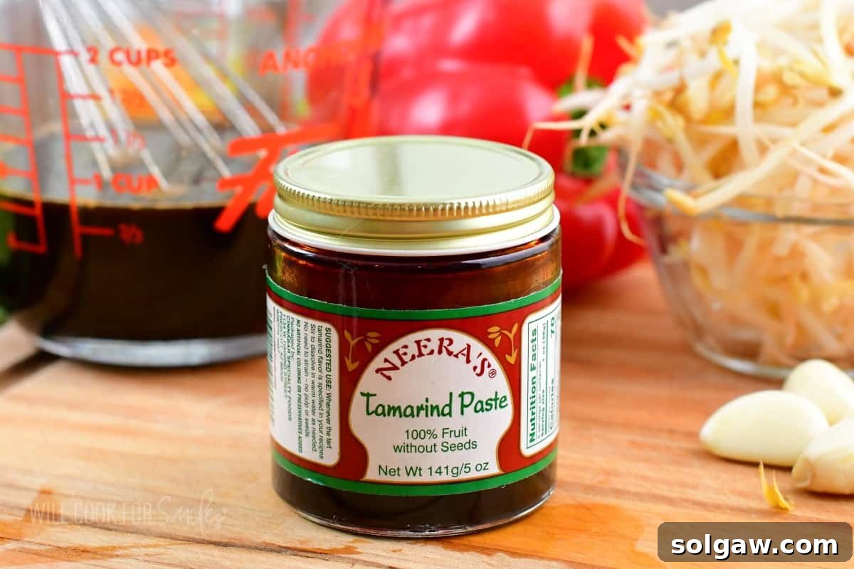 tamarind paste in a small jar on a cutting board with veggies and sauce around.