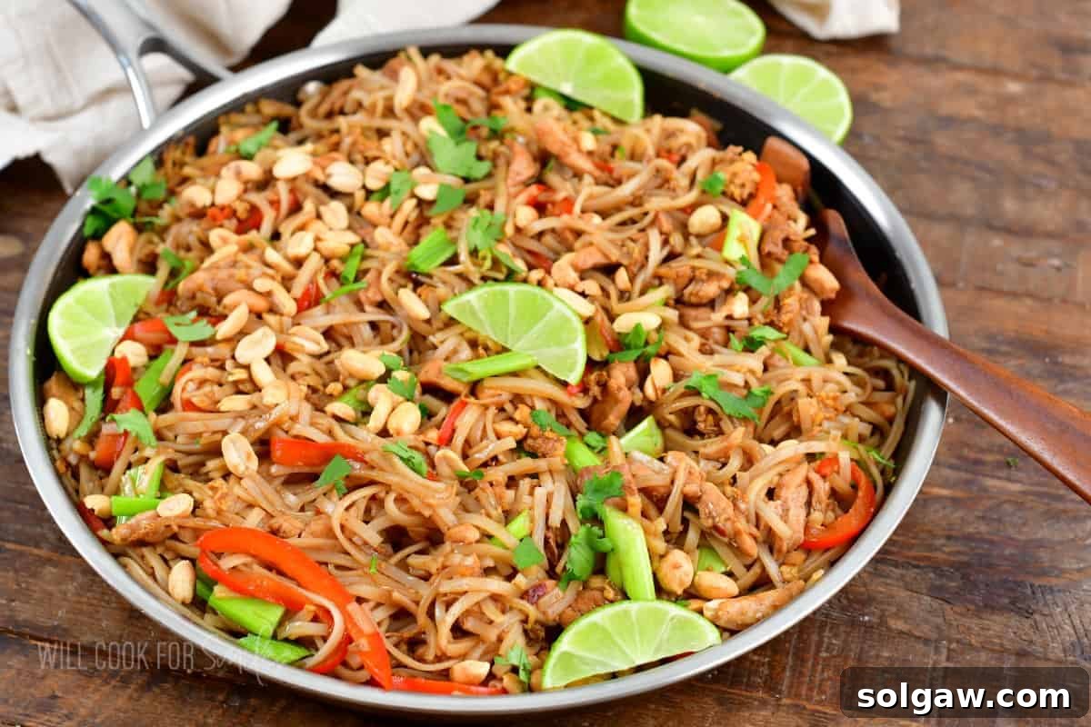 A wooden spoon is placed in a skillet filled with garnished pad Thai.