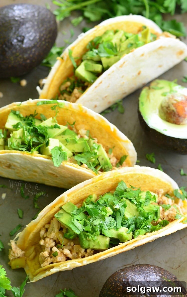 A trio of Avocado Turkey Tacos, each brimming with ground turkey, avocado slices, and cilantro, artfully arranged in hard shells