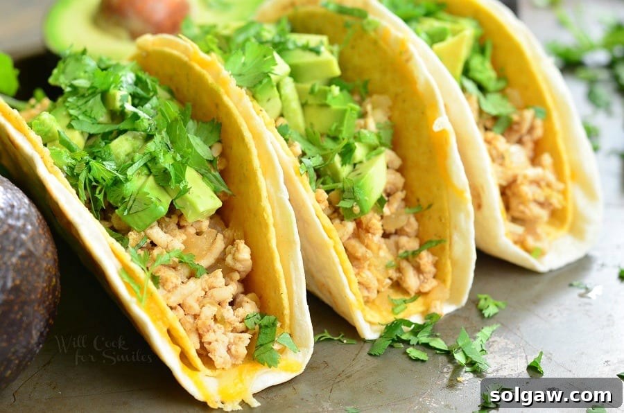 Three Avocado Turkey Tacos in a hard shell, featuring ground turkey, creamy avocado, and fresh cilantro, displayed on a rustic wooden surface