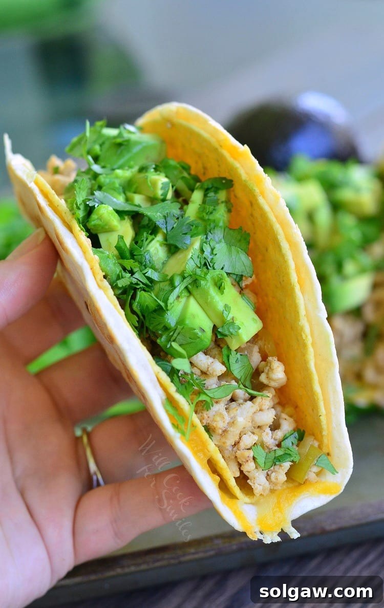 A hand holding an Avocado Turkey Taco with visible ground turkey, avocado slices, and cilantro in a crunchy shell
