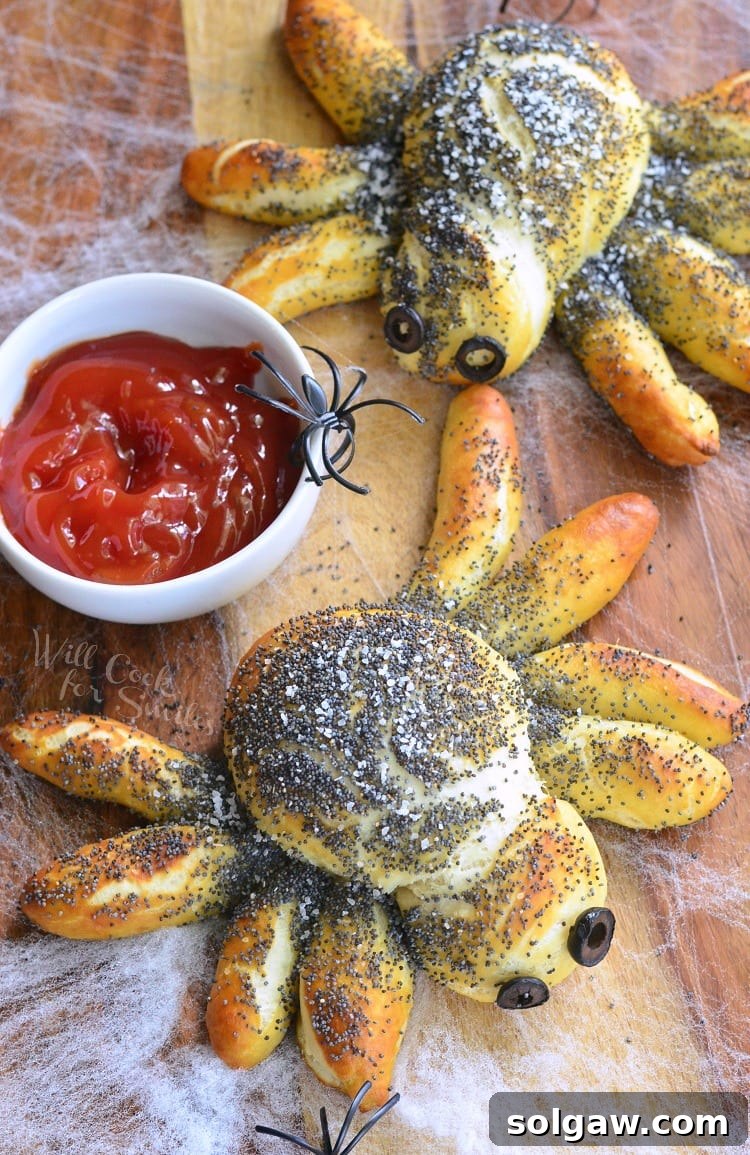 Top view of Pretzel Spiders with olive eyes and a bowl of dipping sauce, surrounded by fake spiders on a white surface.