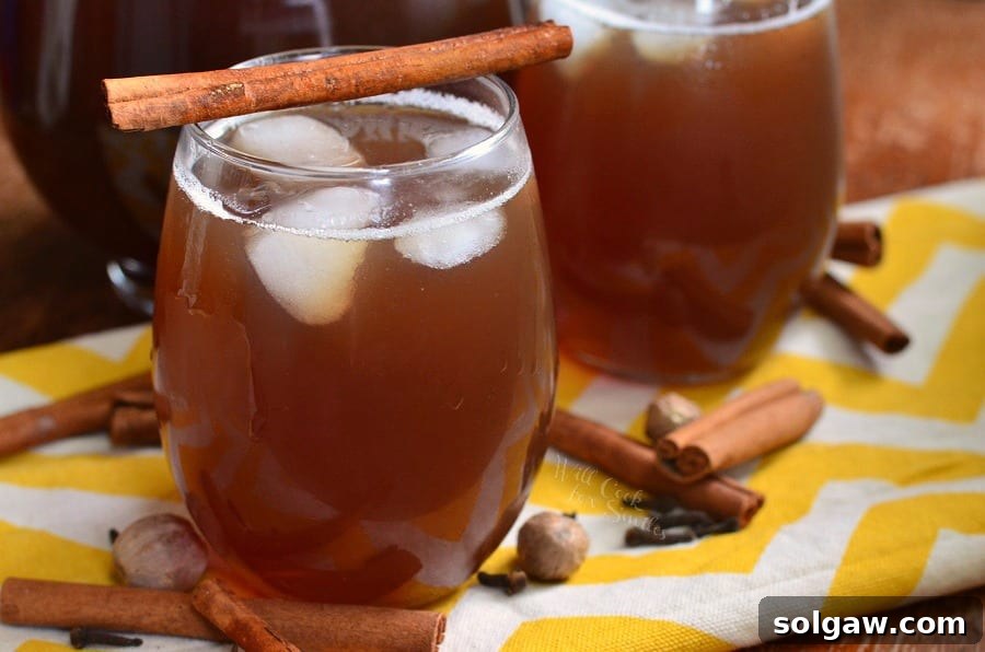 Close-up of a glass of spiced iced tea with ice and a cinnamon stick, showcasing the rich color and inviting condensation on the glass. Spices are scattered around.