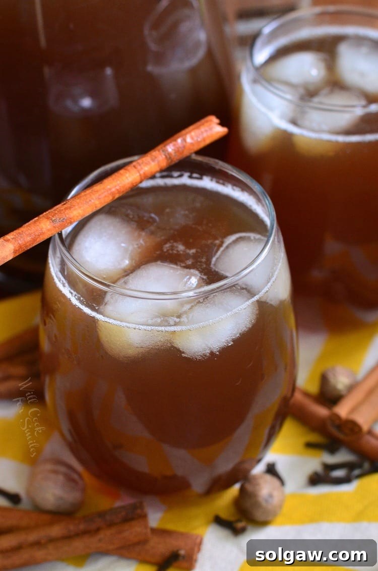 A beautifully presented glass of spiced iced tea, with ice and a cinnamon stick, against a backdrop of warm autumnal colors and cozy textures.
