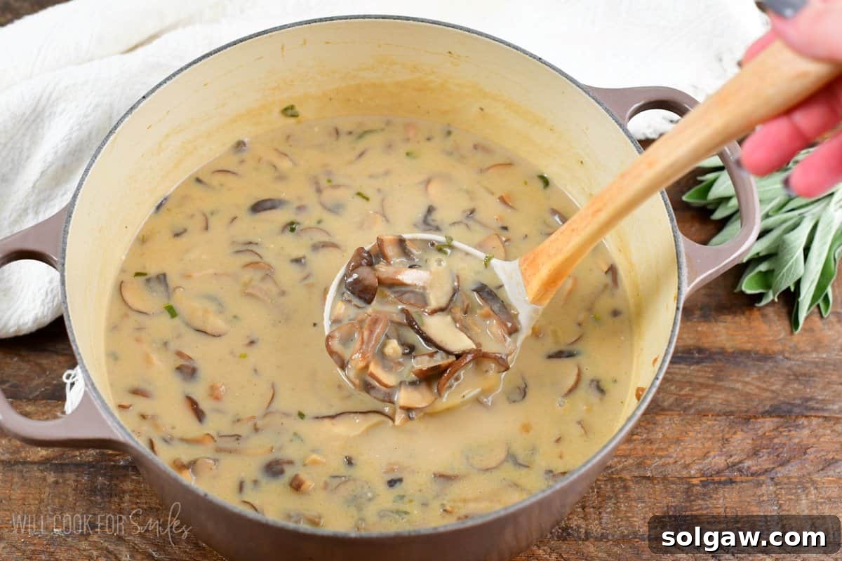 A ladle scooping rich, creamy mushroom soup directly from a large cooking pot, ready to be served.