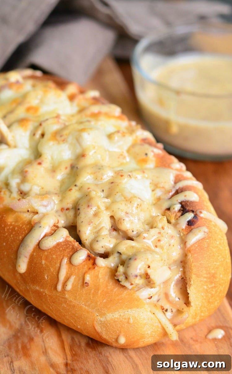 Delicious White BBQ Chicken Sub on a rustic wooden table, accompanied by a bowl of clear BBQ sauce.