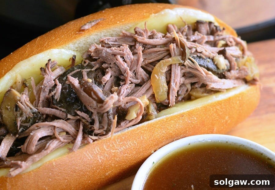 Large hoagie roll covered in cheese, generously filled with slow cooker mushroom and onion Italian beef, resting on a wooden table.